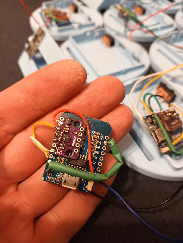 📷 На ладони — другая плата SlimeVR трекера: фиолетовая PCB с USB-micro разъёмом и проводами. На заднем плане — корпуса и другие платы.