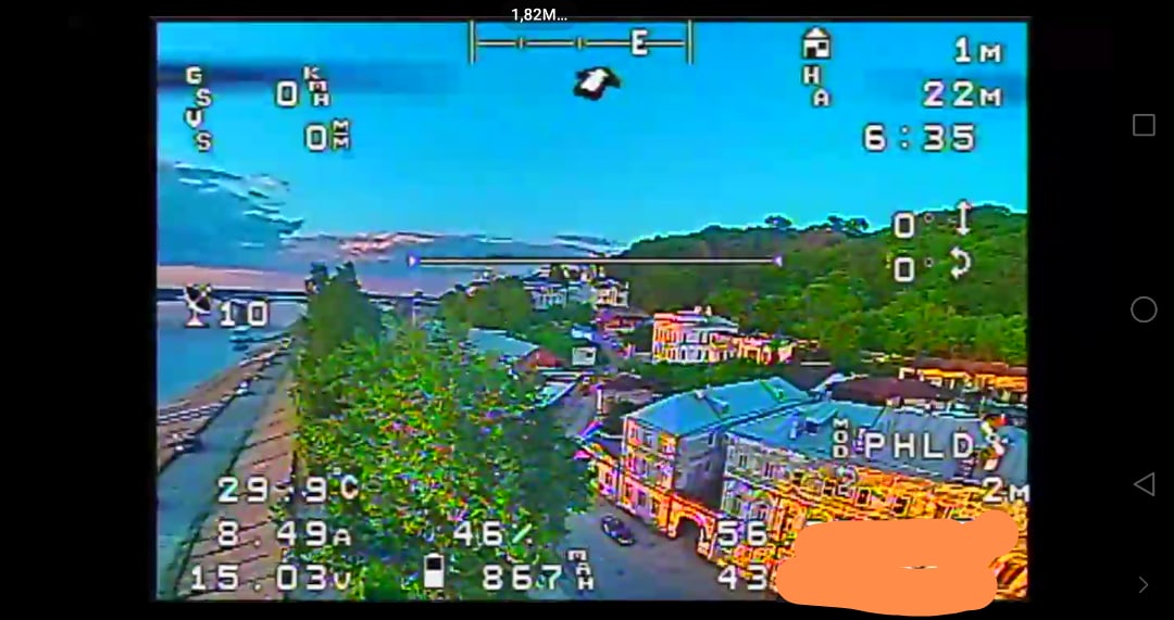 Фото экрана телефона с FPV-трансляцией дрона над набережной и рекой с мостом на закате; OSD: «1.82M / GS 0 / HA 1m / 22M / 6:35 / 29.9°C / 8.49A / 15.03V / 46% / 867m / PHLD / 2m / 56 / 43»