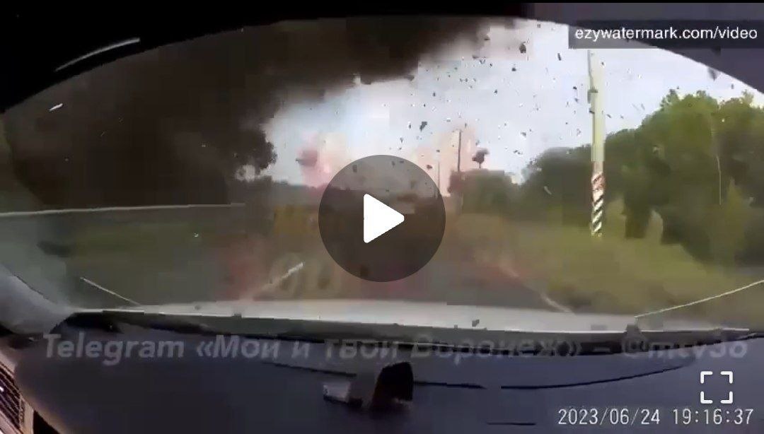 📷 Скриншот видео с видеорегистратора (ezywatermark.com/video): вид через лобовое стекло автомобиля — впереди клубы дыма, вспышка взрыва, летящие осколки; деревья и дорога видны сквозь дым; надпись внизу: «Telegram «Мой и твой Воронеж»»; дата/время: 2023/06/24 19:16:37.