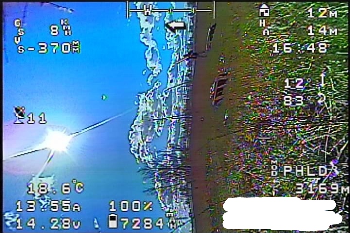 Скриншот FPV-трансляции перед падением: OSD — «GS 8W / S -370A / ↑ 11 / 18.6°C / 13:55A / 100% / 14.28V / 7284mAh / 12m / H=14m / 16:48 / PHLD / 3169» — горизонт резко перекошен, земля и деревья снизу