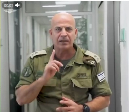📋 Кадр видео (00:05): израильский военный в форме с флагом Израиля на рукаве, поднятый указательный палец вверх.