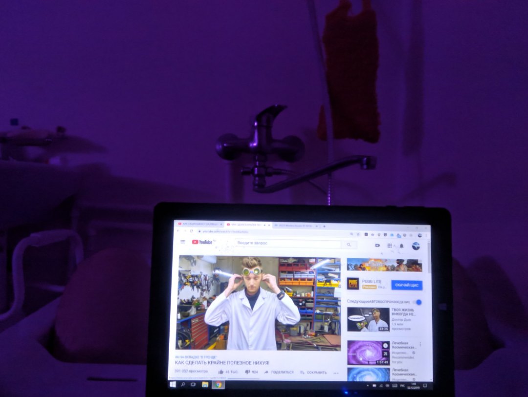 Ноутбук в ванной комнате с фиолетовой подсветкой: тот же YouTube — «КАК СДЕЛАТЬ КРАЙНЕ ПОЛЕЗНОЕ НИХУЯ», крупнее; кран, стены ванной